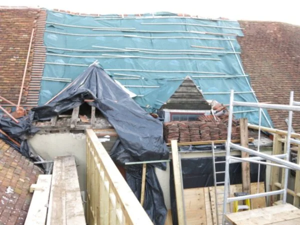 Rooftop with polythene overlay on missing roof tiles surrounded by scaffolding