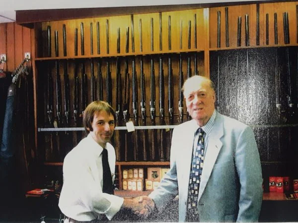 shop owners sharing a handshake in front of gun cabinet